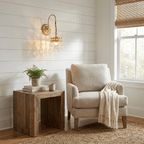 A Clérachic crystal-drop wall light on a shiplap wall, glowing above a rustic side table and a cream armchair with a knitted throw.