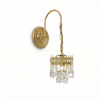 Angled view of this Clérachic wall light, its curved arm, chain and crown of clear crystal drops hanging below an embossed round backplate.