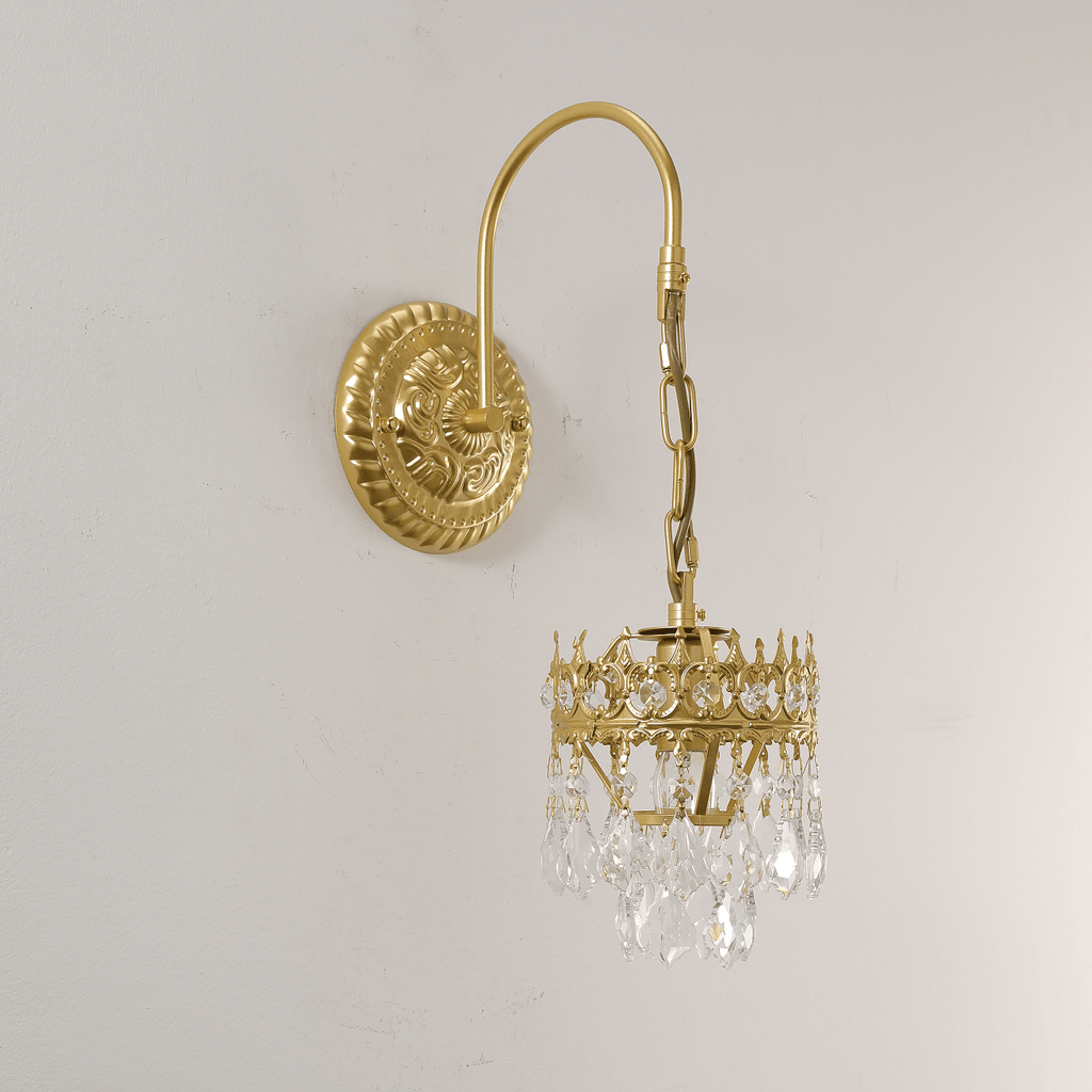 Close view of the clear crystal drops and crown-shaped frame on this Clérachic wall sconce, mounted on a soft off-white wall.