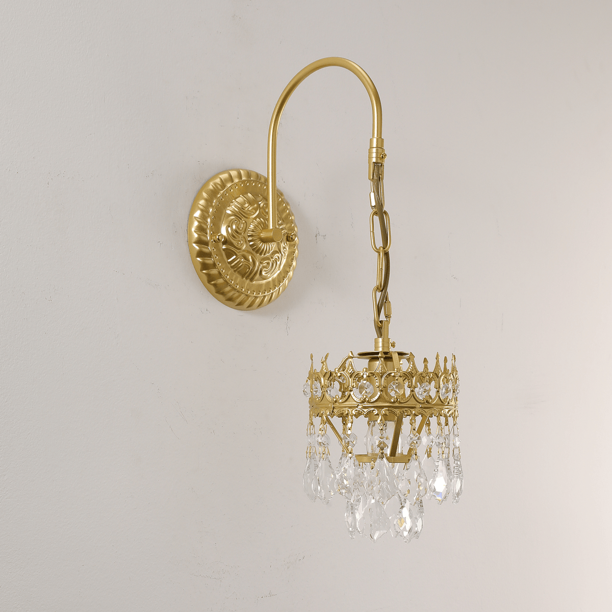 Close view of the clear crystal drops and crown-shaped frame on this Clérachic wall sconce, mounted on a soft off-white wall.