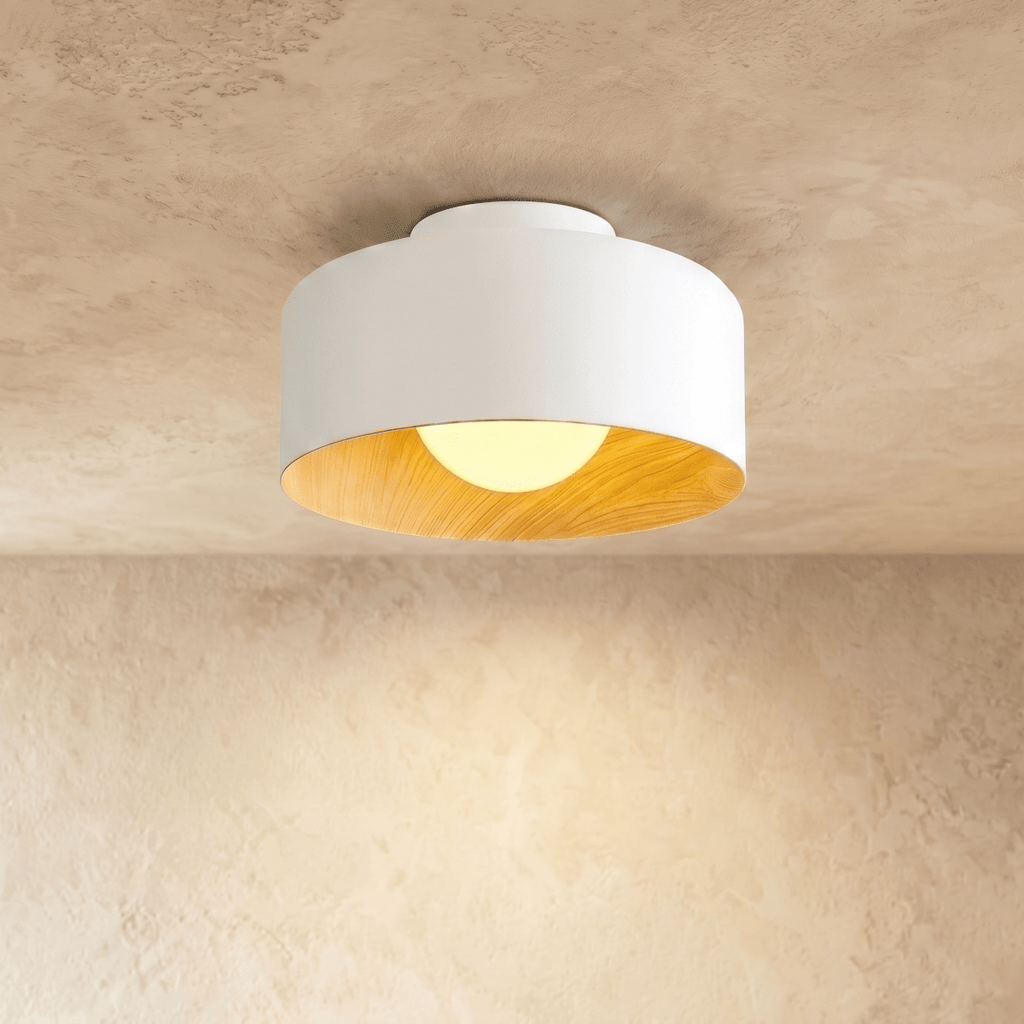 Clérachic white metal drum ceiling light with a wood-grain interior and an opal ball glowing warm, on a limewashed ceiling.