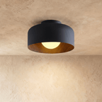 Clérachic matt black drum ceiling light with a wood-grain interior and a softly lit opal ball, on a limewashed ceiling.