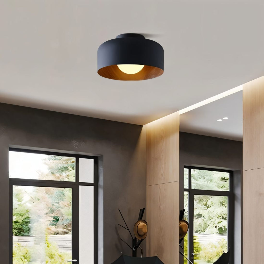Clérachic black drum ceiling light hung in a hallway with timber panelling, a coat stand and tall windows beyond.