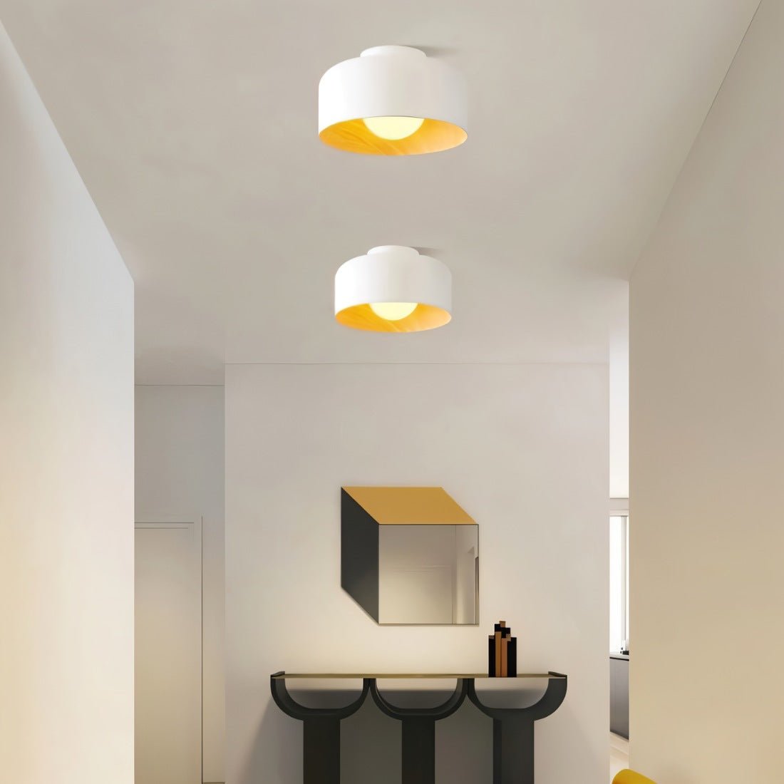 Clérachic pair of white drum ceiling lights with wood interiors above a corridor, a hexagonal mirror and a black console.