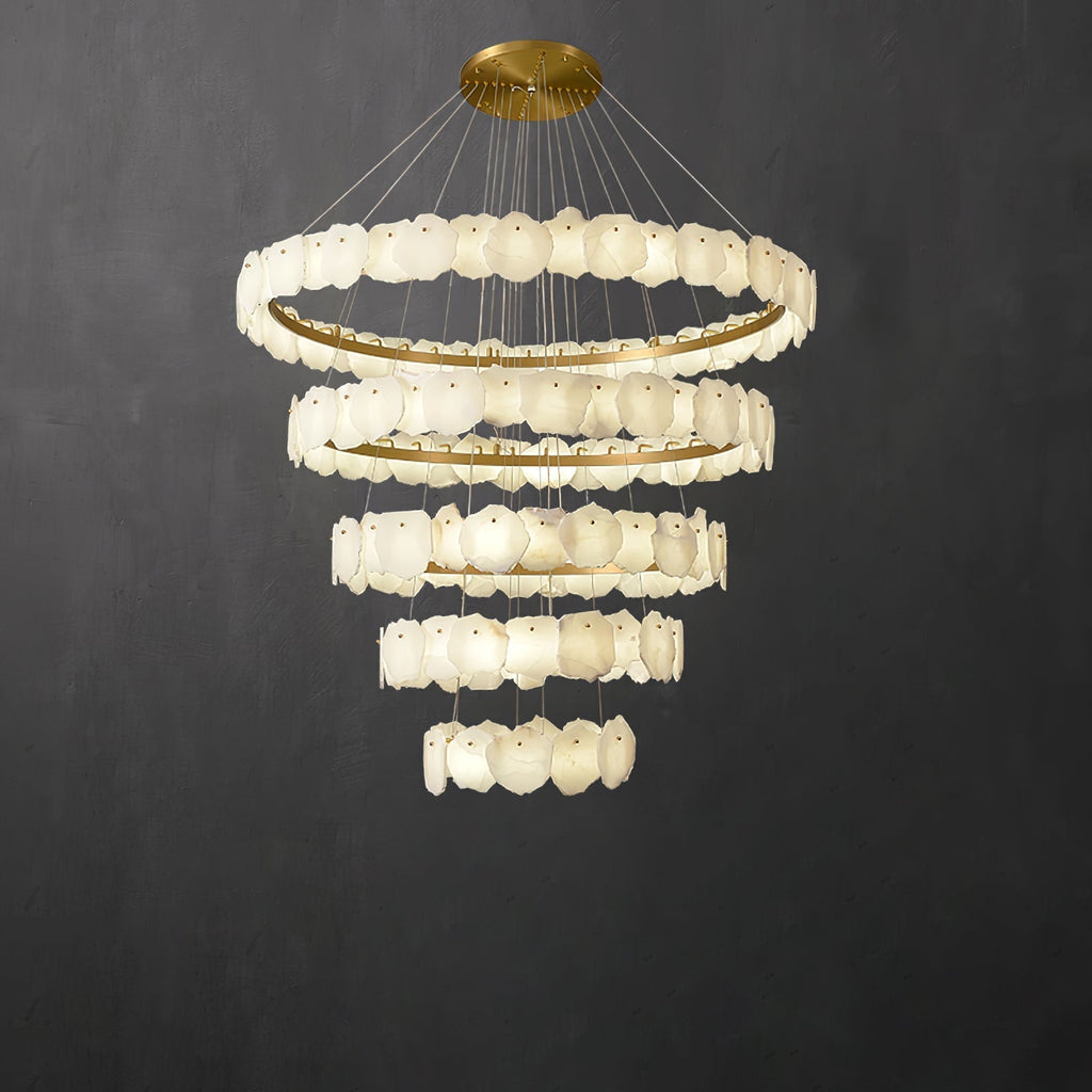 The Clérachic Ecliptica alabaster chandelier lit against a dark grey wall, tiers tapering downward.