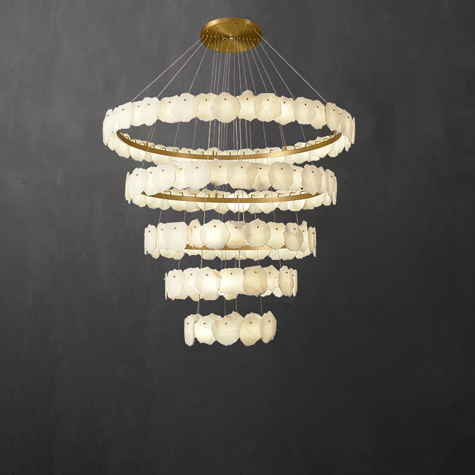 The Clérachic Ecliptica alabaster chandelier lit against a dark grey wall, tiers tapering downward.