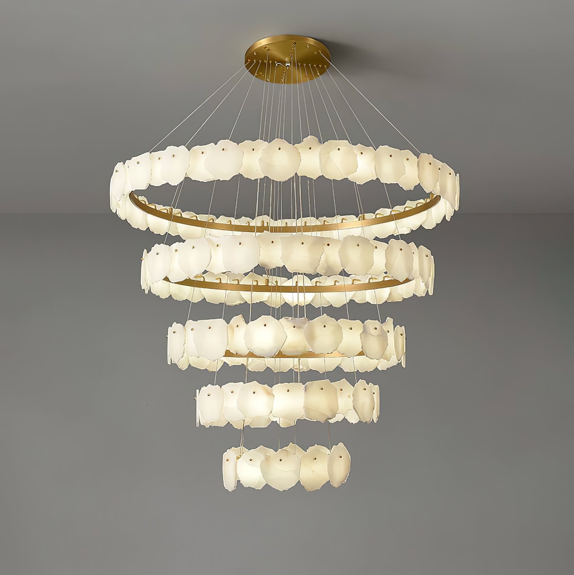 Clérachic Ecliptica chandelier seen from below against a pale ceiling, brass rings glowing warm.
