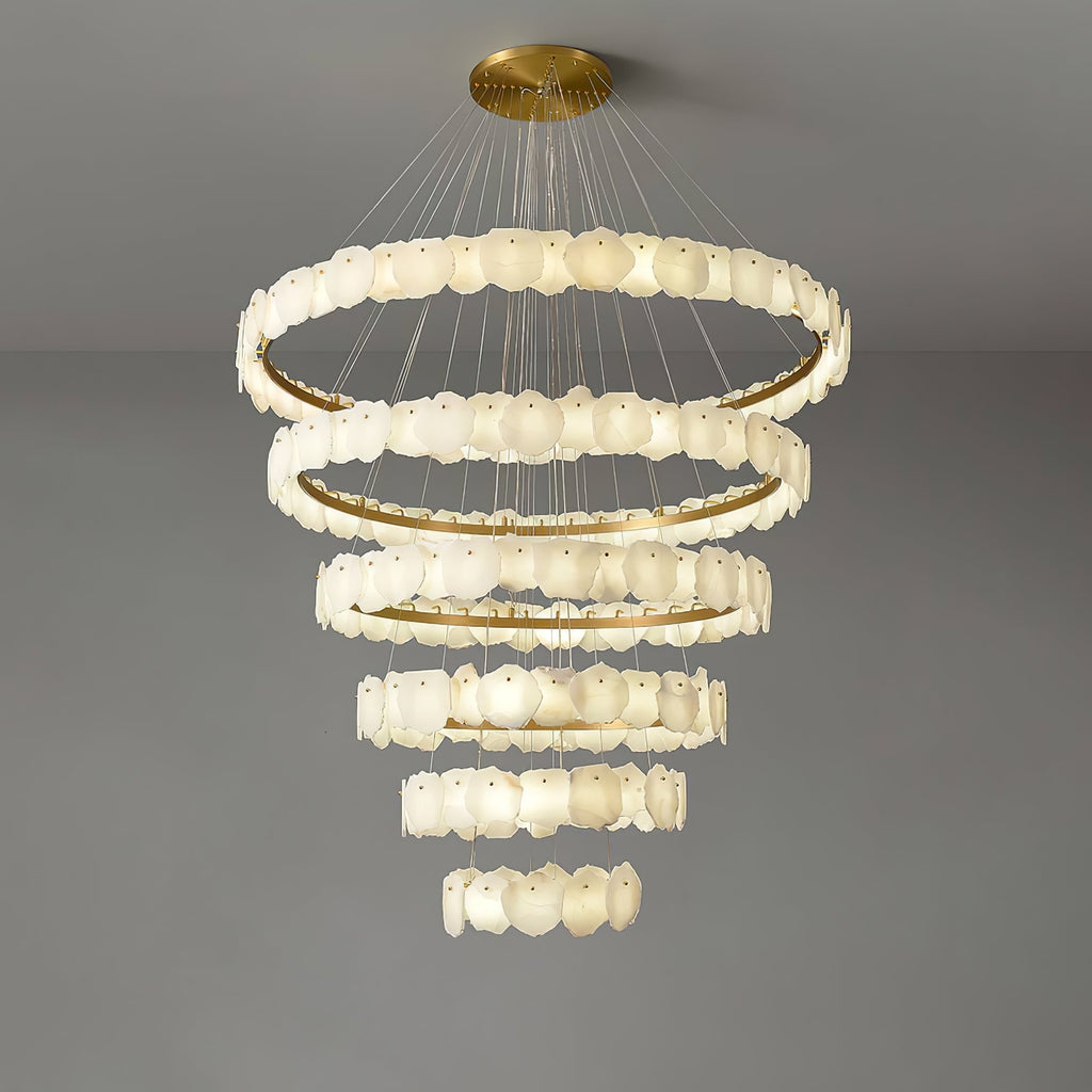 The Clérachic Ecliptica chandelier lit on grey, warm light washing across the layered petals.