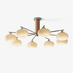 Eight-light chandelier from Clérachic with creamy yellow glass shades on chrome arms around a wooden centre column, on a plain white backdrop.