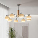 Lit chandelier from Clérachic with chrome arms and creamy glass shades hung in a bright living room, with a tall grass plant and soft curtains beside it.