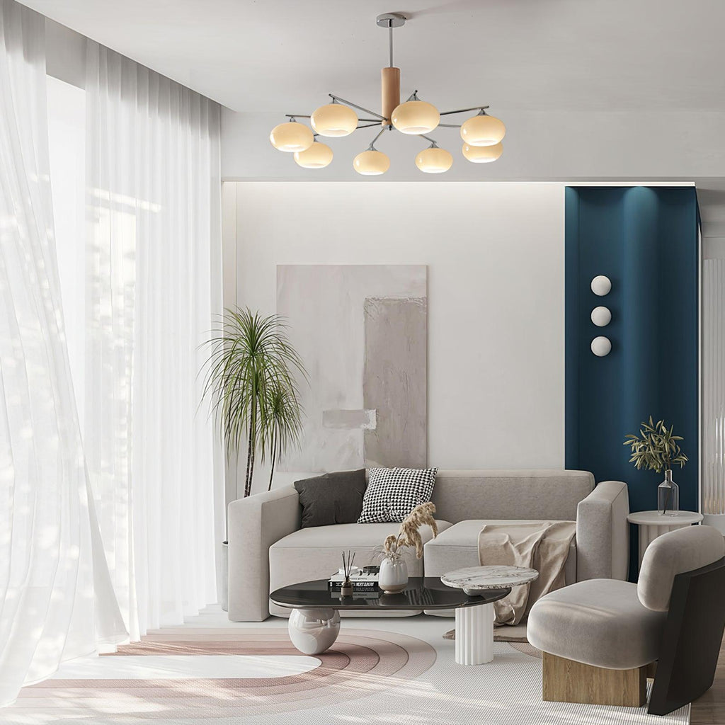 Clérachic chandelier with creamy glass shades hanging over a pale living room with a grey sofa, a round coffee table and a teal accent wall.