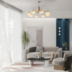 Clérachic chandelier with creamy glass shades hanging over a pale living room with a grey sofa, a round coffee table and a teal accent wall.