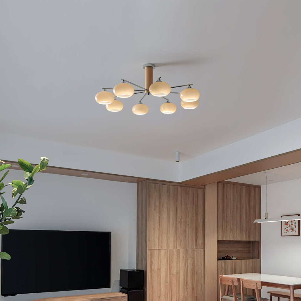 A Clérachic chandelier seen from across an open room with wood panelling, a wall-mounted television and a dining table in the distance.