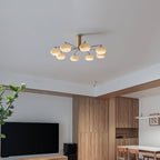 A Clérachic chandelier seen from across an open room with wood panelling, a wall-mounted television and a dining table in the distance.