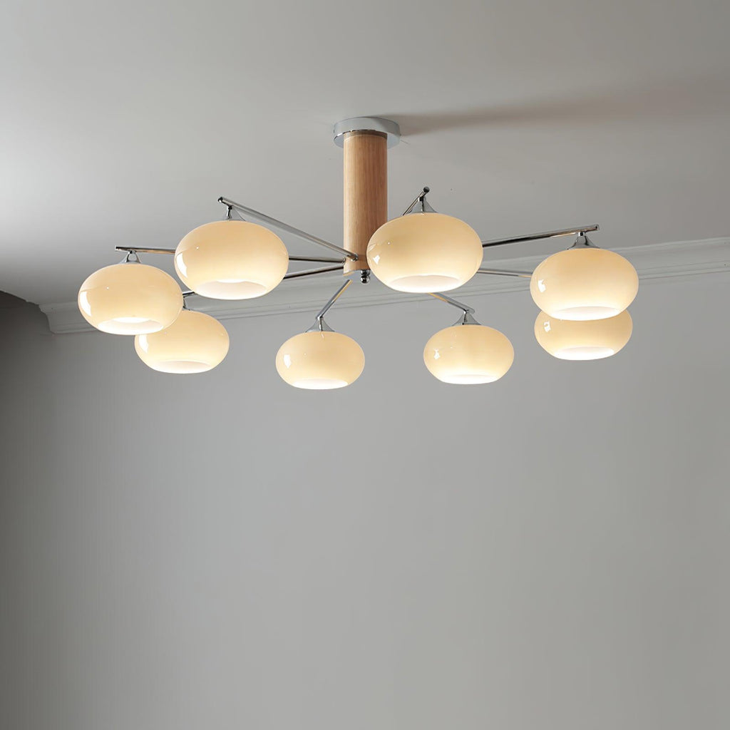 Chandelier from Clérachic with creamy glass shades and a wooden column, lit against a plain grey ceiling and wall.