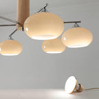 Close view of three rounded creamy glass shades on this Clérachic chandelier, with a small lit pendant resting on the floor below.