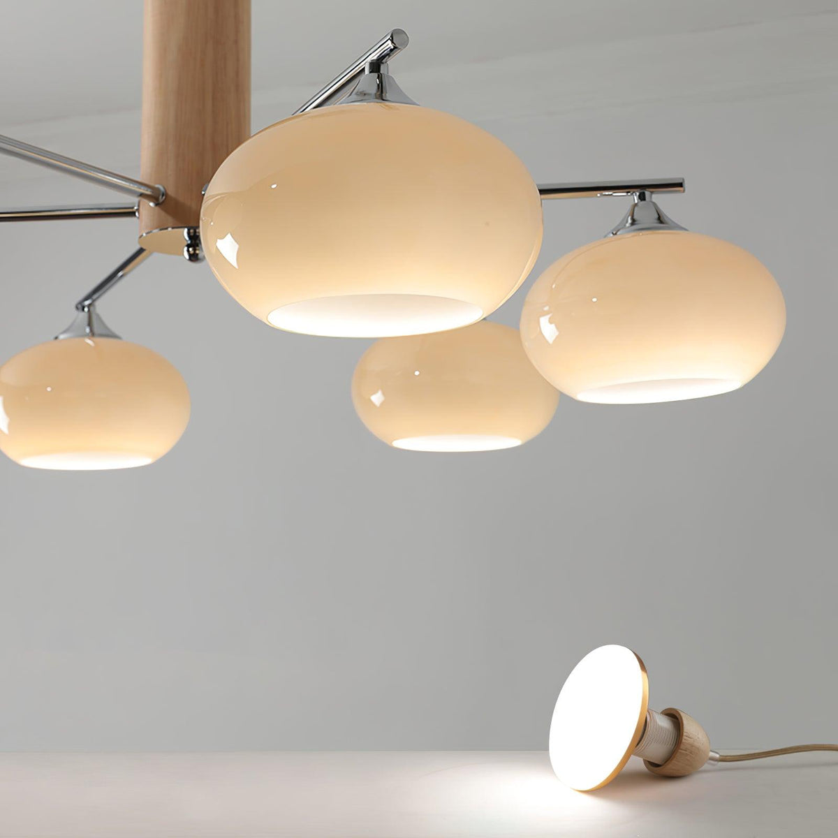 Close view of three rounded creamy glass shades on this Clérachic chandelier, with a small lit pendant resting on the floor below.