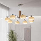 Clérachic chandelier with creamy glass shades hung above a living room corner, with a tall grass plant and a soft abstract wall panel.
