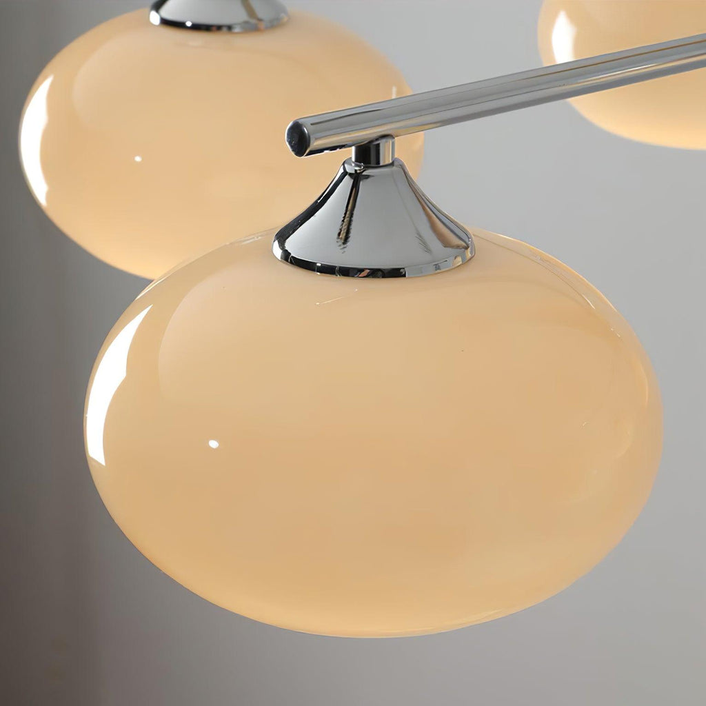 Close view of a rounded creamy glass shade held by a chrome cone cap on a chrome arm of this Clérachic chandelier.