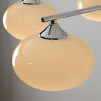 Close view of a rounded creamy glass shade held by a chrome cone cap on a chrome arm of this Clérachic chandelier.