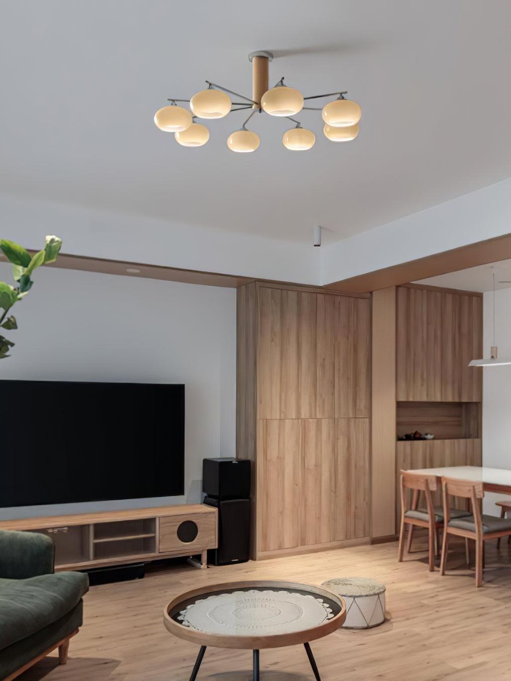 Distant view of a lit Clérachic chandelier on a high ceiling above a wood-panelled room with a television and a dining table.