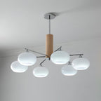 Lit chandelier from Clérachic with milk white glass shades giving a cool white glow, hung from a chrome rod below a plain ceiling.