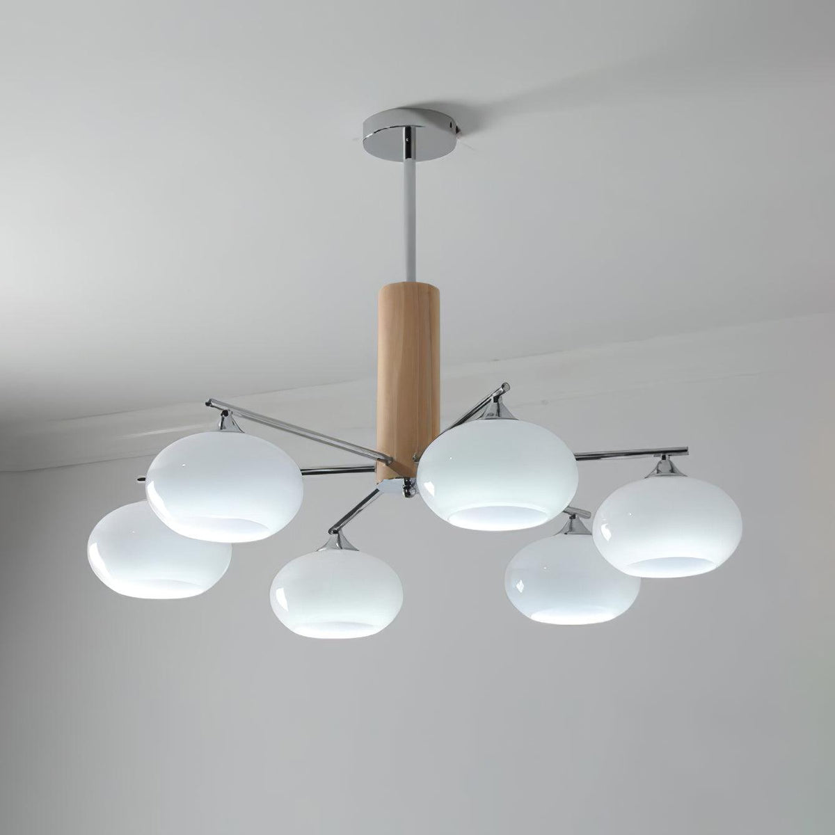 Lit chandelier from Clérachic with milk white glass shades giving a cool white glow, hung from a chrome rod below a plain ceiling.