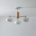 Three-light chandelier from Clérachic with milk white glass shades on chrome arms and a wooden column, below a white ceiling.