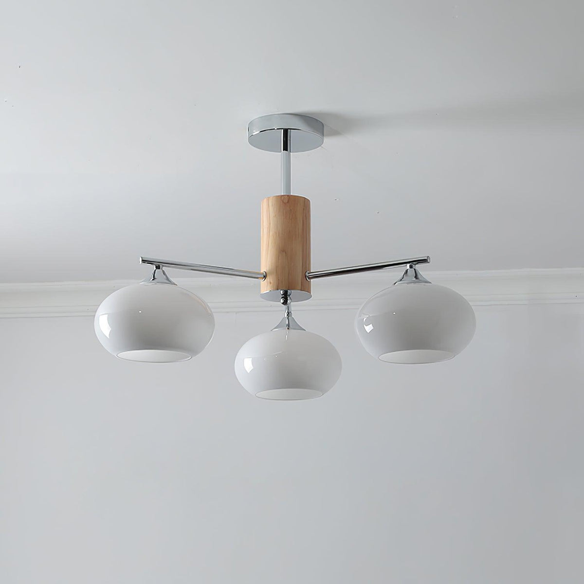 Three-light chandelier from Clérachic with milk white glass shades on chrome arms and a wooden column, below a white ceiling.