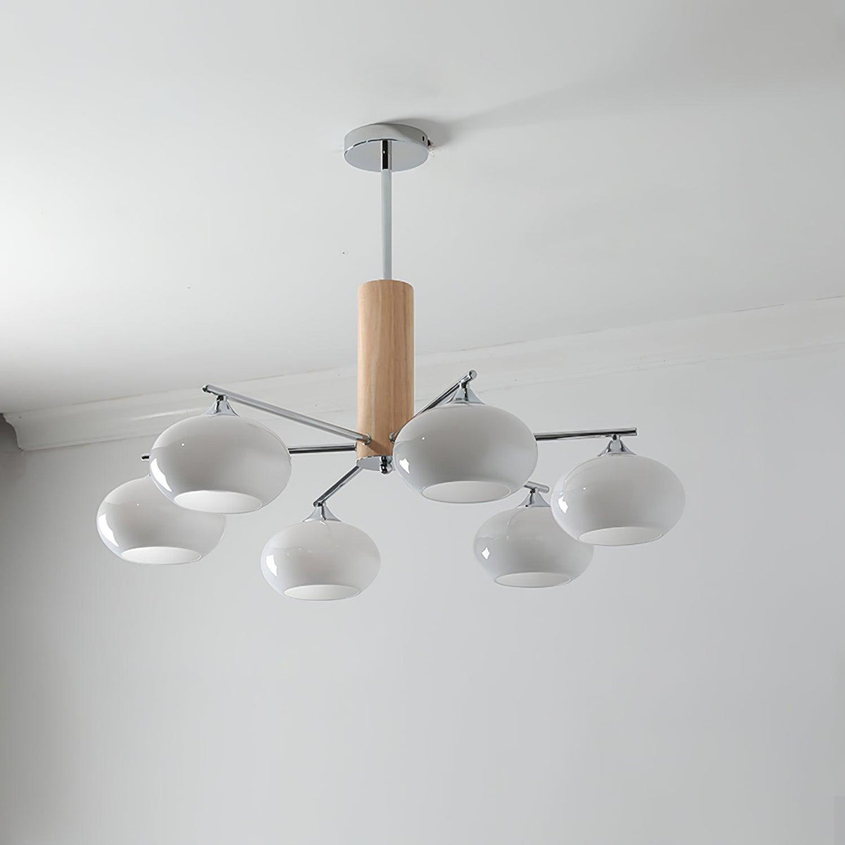 Five-light chandelier from Clérachic with milk white glass shades on chrome arms, unlit, hung from a chrome rod below a grey ceiling.