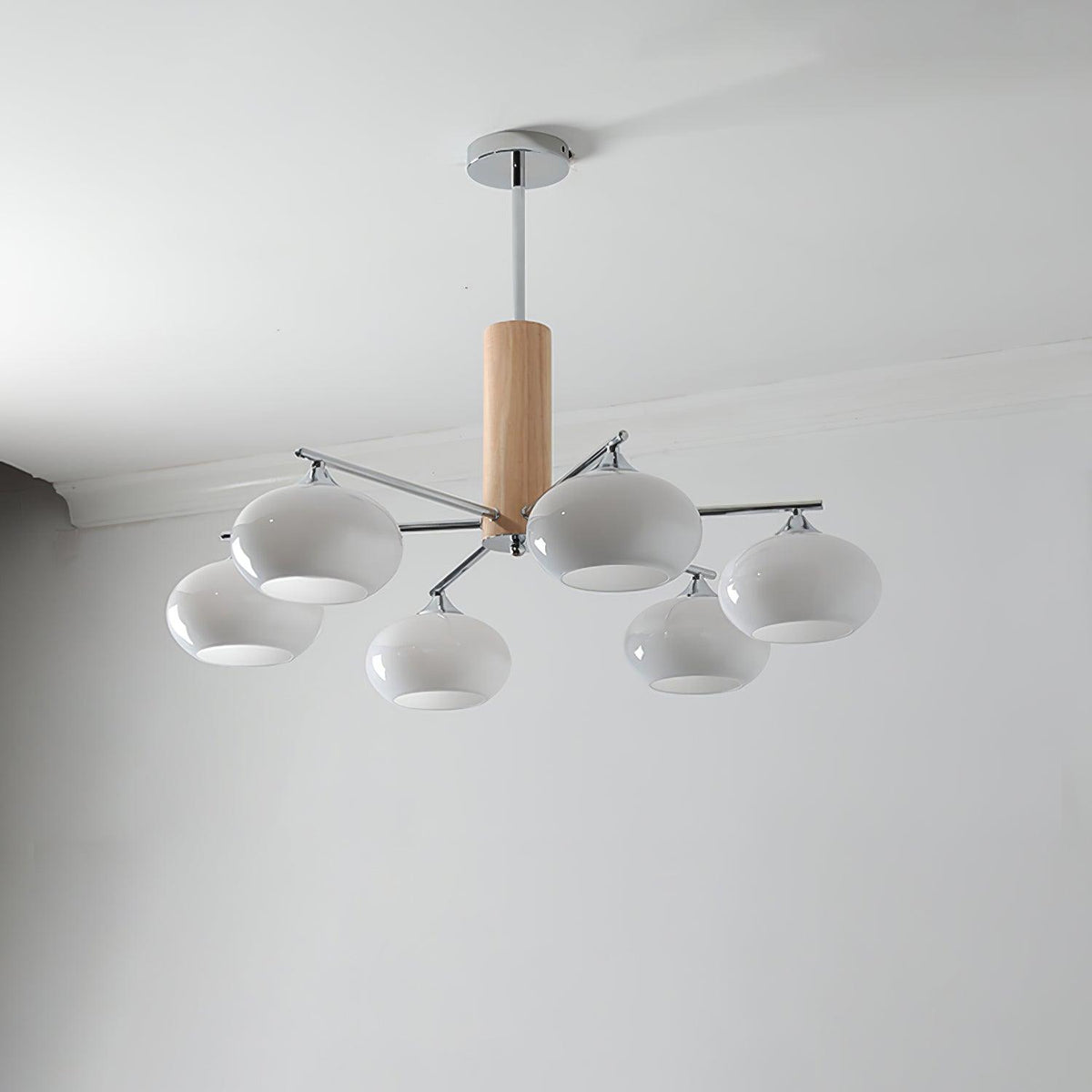 Unlit chandelier from Clérachic with milk white rounded glass shades, a wooden column and a chrome canopy on a pale grey wall.