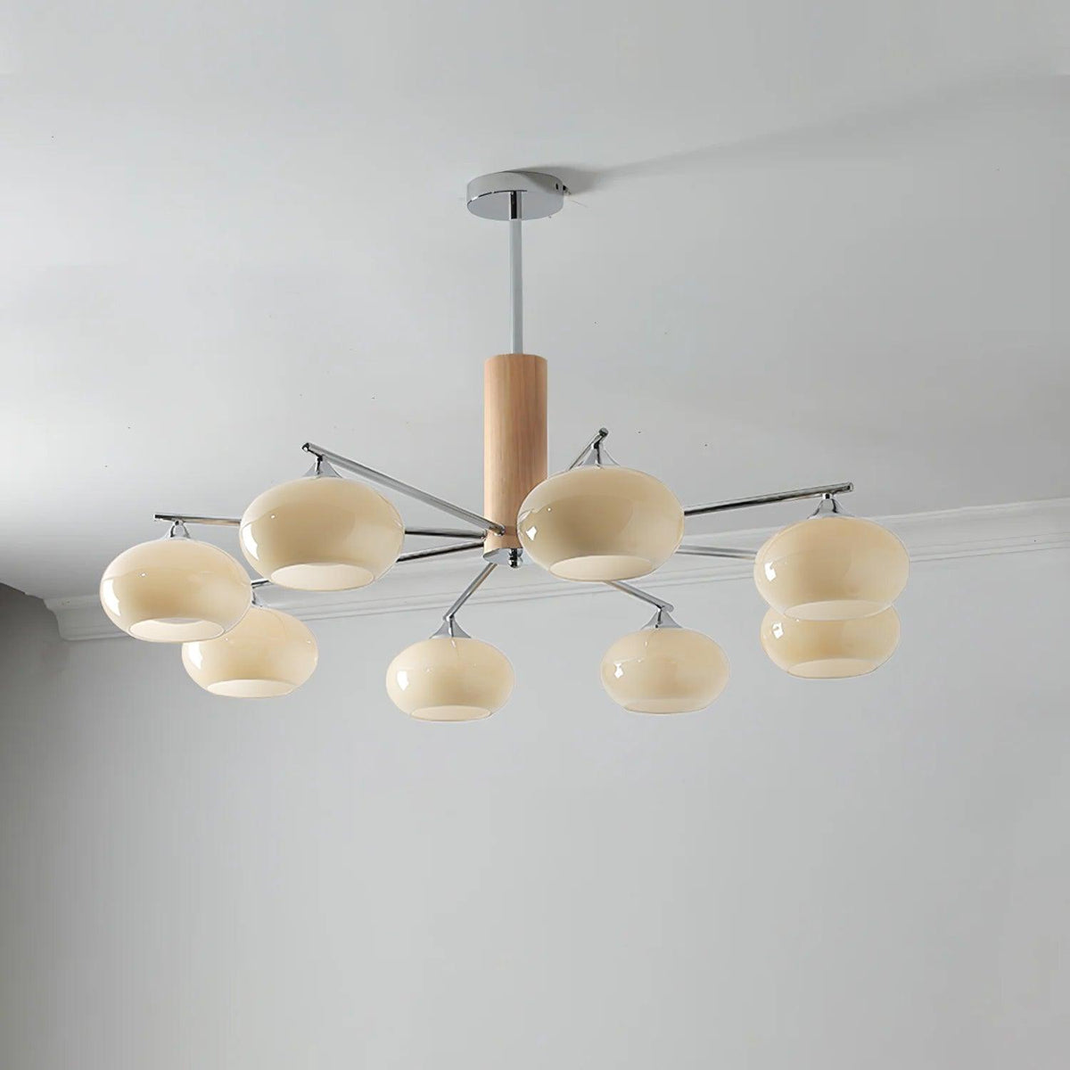 Lit Clérachic chandelier with eight creamy glass shades on chrome arms, hung from a rod below a grey ceiling with a white cornice.