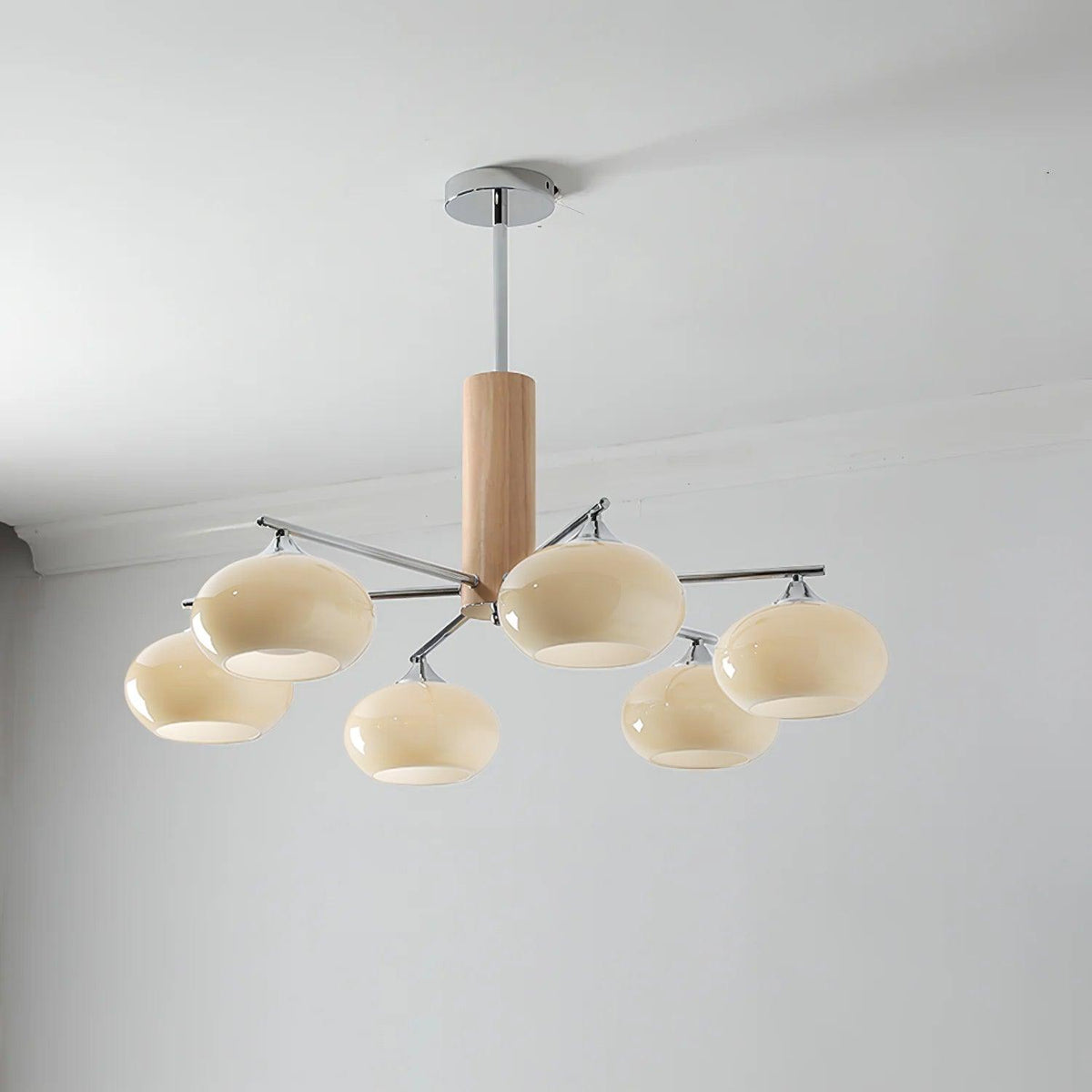 Six-light chandelier from Clérachic with creamy glass shades glowing softly, hung from a chrome rod near a white cornice.