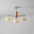 Three-light chandelier from Clérachic with wide creamy yellow glass shades on chrome arms, hung below a grey ceiling.