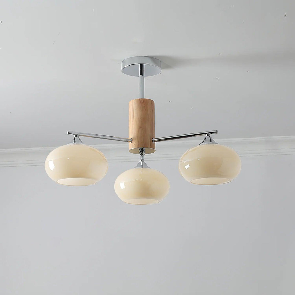 Three-light chandelier from Clérachic with wide creamy yellow glass shades on chrome arms, hung below a grey ceiling.