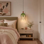 This Clérachic pendant with an olive shade and pale fringe hangs by a bed with blush linen, above a small wooden nightstand.