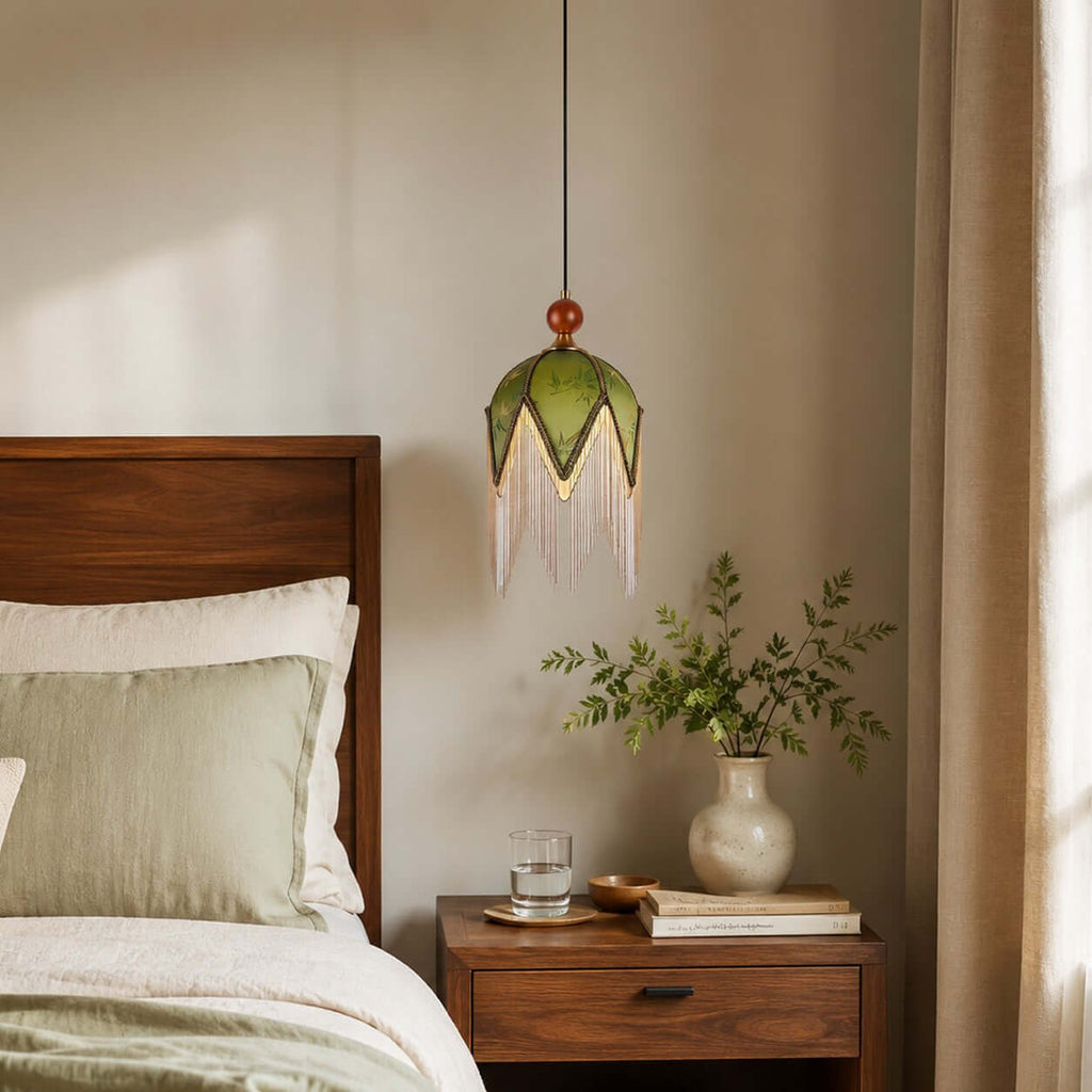 Olive-green fabric panels and a soft bead fringe on this Clérachic pendant, hung beside a walnut bed and a vase of leaves.