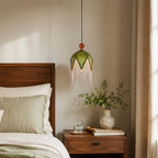 Olive-green fabric panels and a soft bead fringe on this Clérachic pendant, hung beside a walnut bed and a vase of leaves.