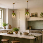 Two olive-shaded Clérachic pendants with pale fringe hang over a kitchen island, with green tiles and a range cooker behind.