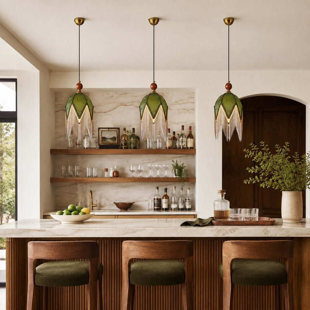 A row of three Clérachic pendants with olive shades hangs above a marble island, in front of open shelves of glasses and bottles.