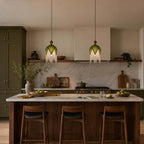 Two Clérachic pendants with green shades and short fringe hang in a dark green kitchen above a walnut island with leather stools.