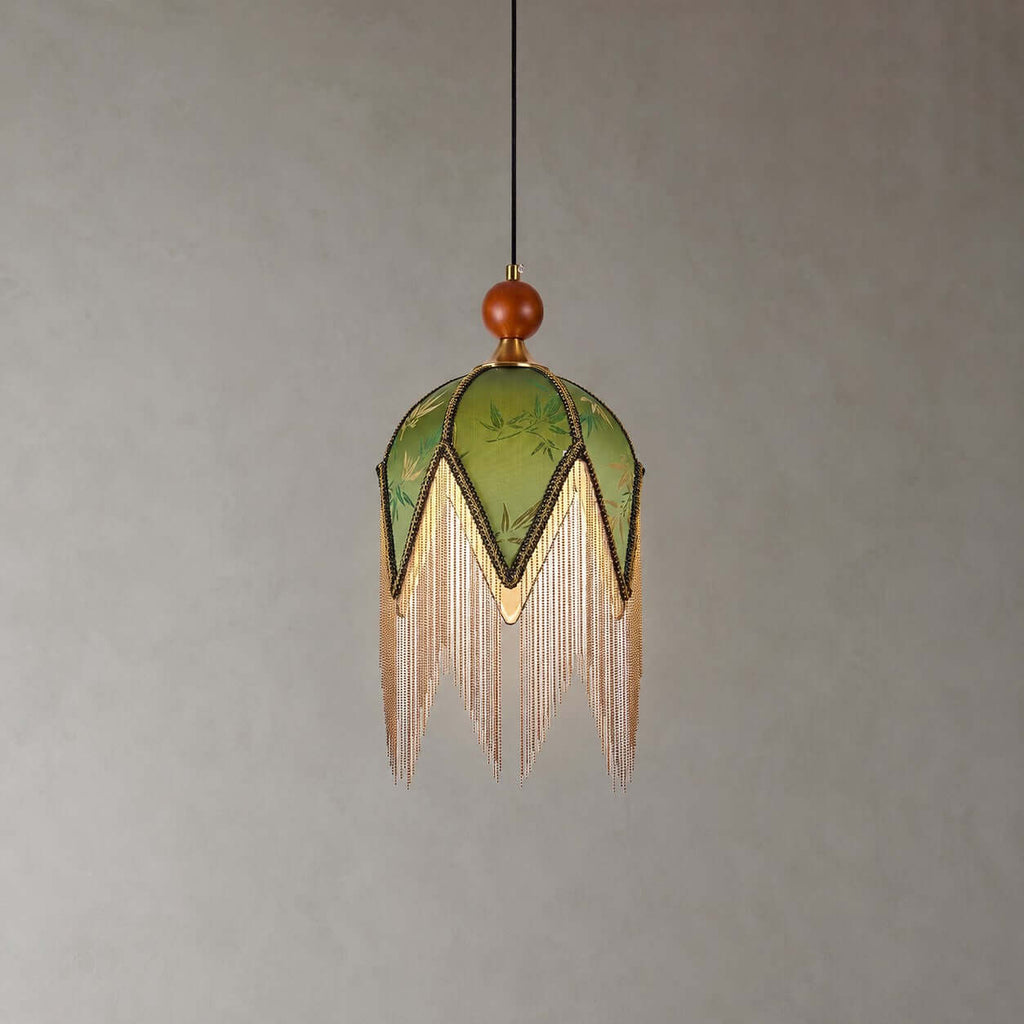 The petal-pointed olive shade of this Clérachic pendant, with a wooden bead at the top and a long fringe, on a grey backdrop.
