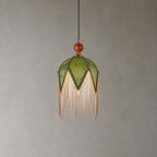 The petal-pointed olive shade of this Clérachic pendant, with a wooden bead at the top and a long fringe, on a grey backdrop.