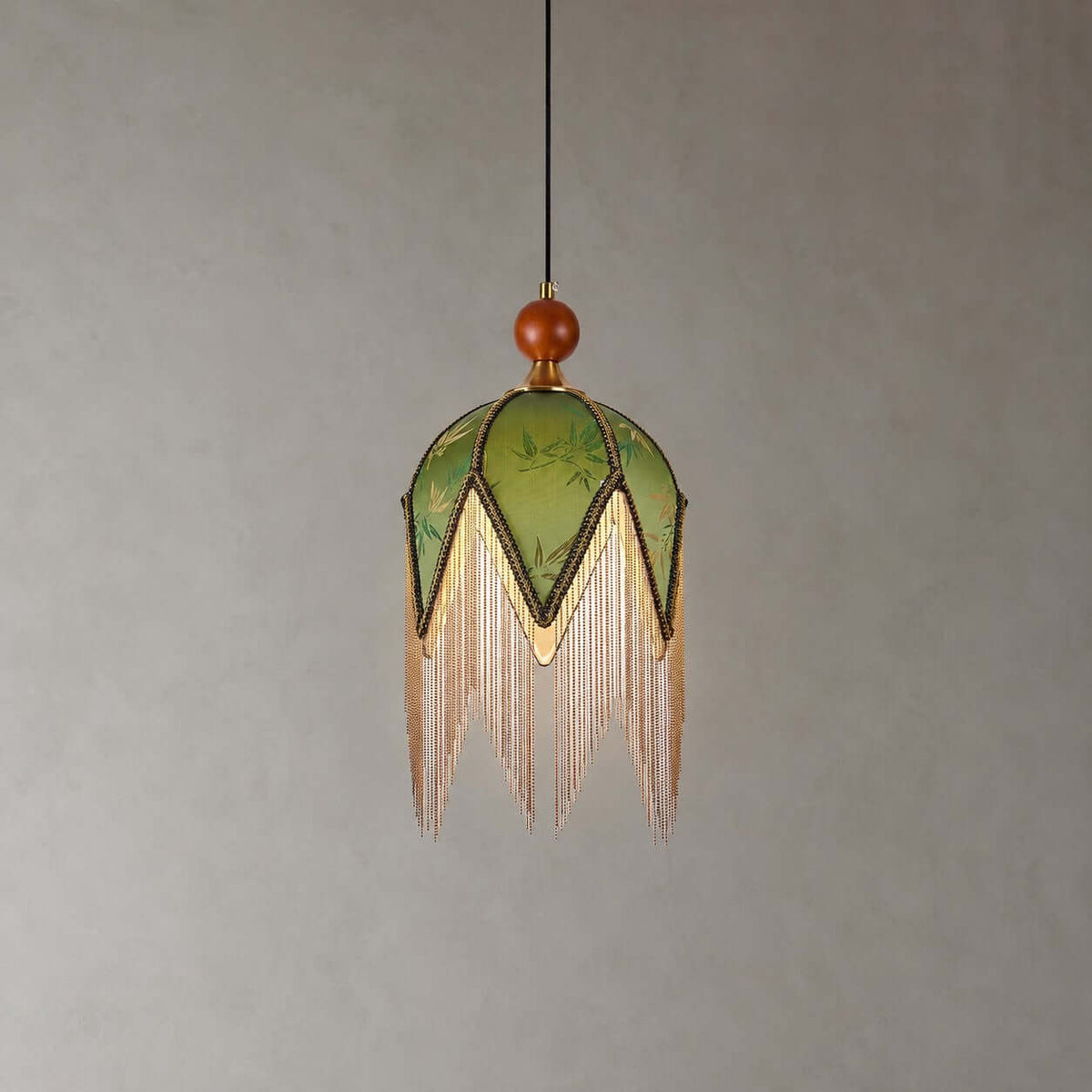 The petal-pointed olive shade of this Clérachic pendant, with a wooden bead at the top and a long fringe, on a grey backdrop.