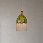 This Clérachic pendant has a scalloped olive dome shade with a straight bead fringe and a wooden finial, on a grey backdrop.