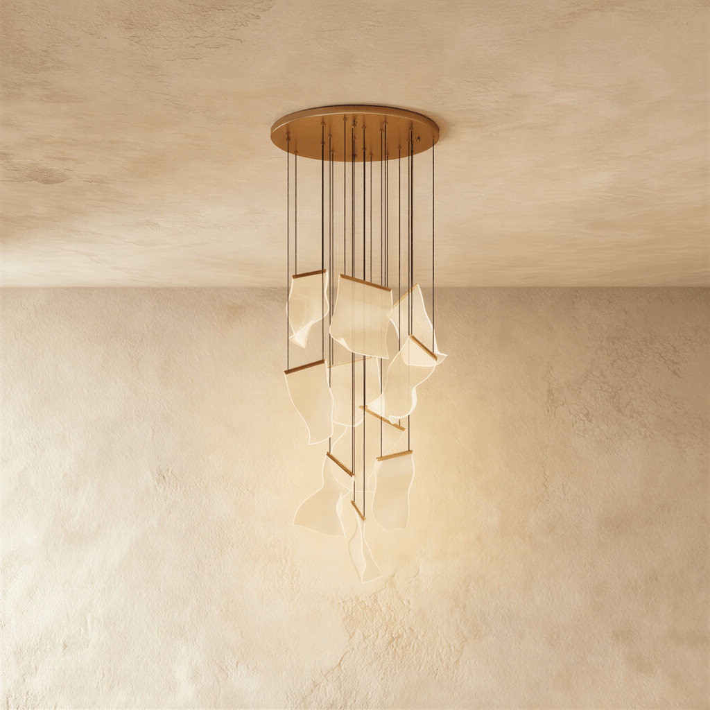 Clérachic gold chandelier shown against a plaster wall, its acrylic panes lit warm on slender hanging cords.