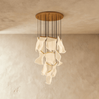 Clérachic gold chandelier showing its tiered brass bars and glowing acrylic sheets against a warm plaster wall.