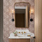 Clérachic's Eris wall lamp flanks a mirror in a dark finish above a marble vanity and floral wallpaper.