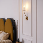 Clérachic's Eris wall lamp lit in brass above a black tufted headboard in a bedroom setting.