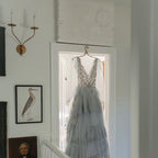 Clérachic's Eris wall lamp in its dark two-arm finish lights a sage-green hallway beside a hanging dress.